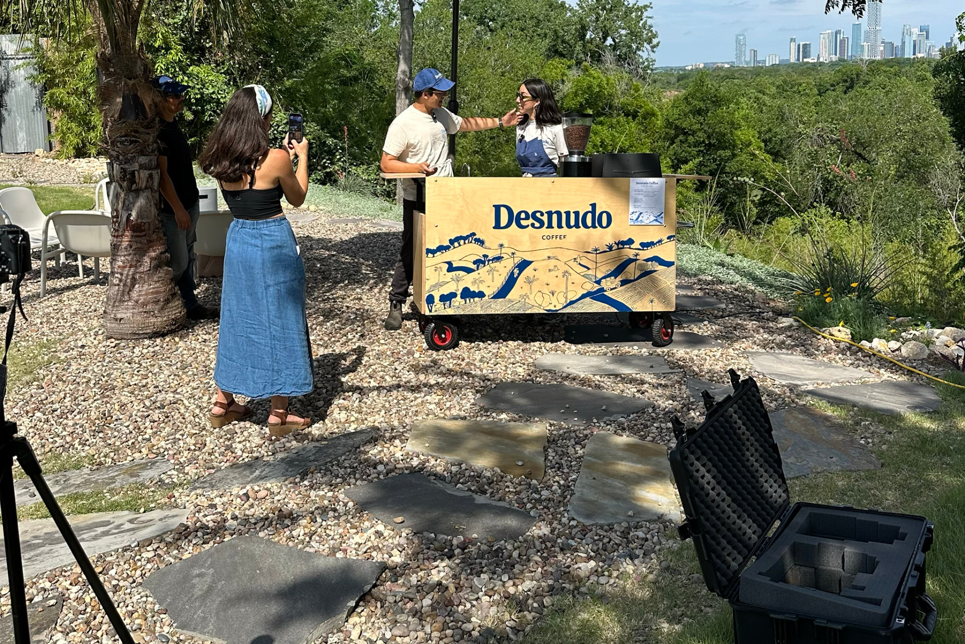 Behind the scenes on a shoot: camera equipment, crew, and the Desnudo coffee cart with the Austin skyline beyond