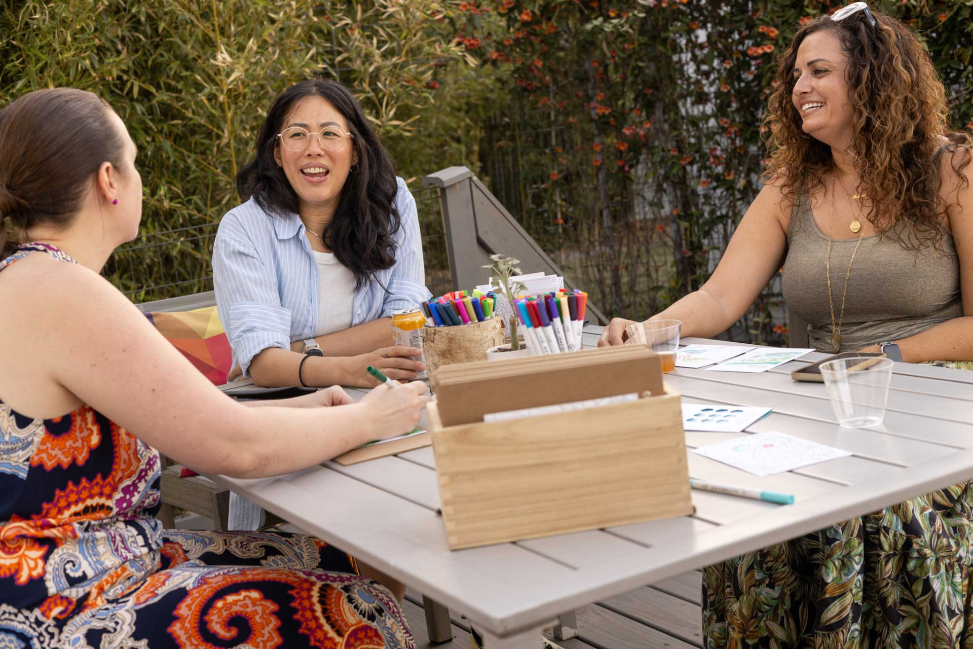 Three guests in conversation around an outdoor table with notebooks and markers