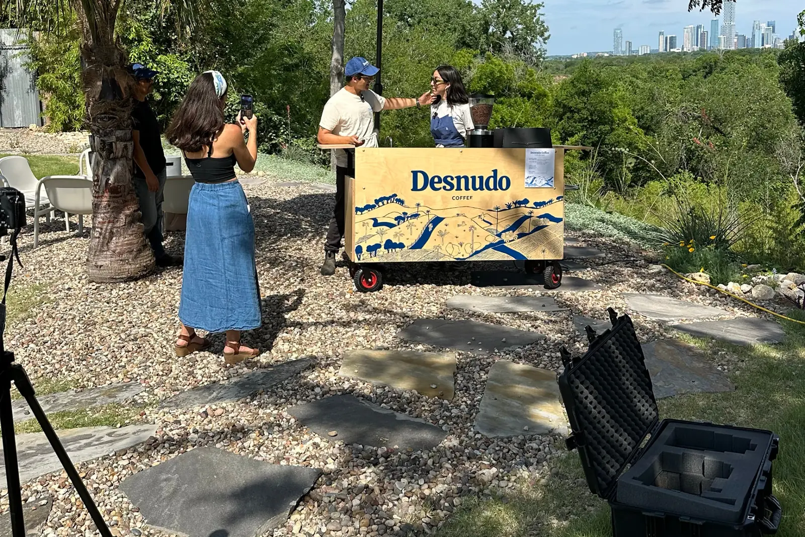 Behind the scenes on a shoot: camera equipment, crew, and the Desnudo coffee cart with the Austin skyline beyond