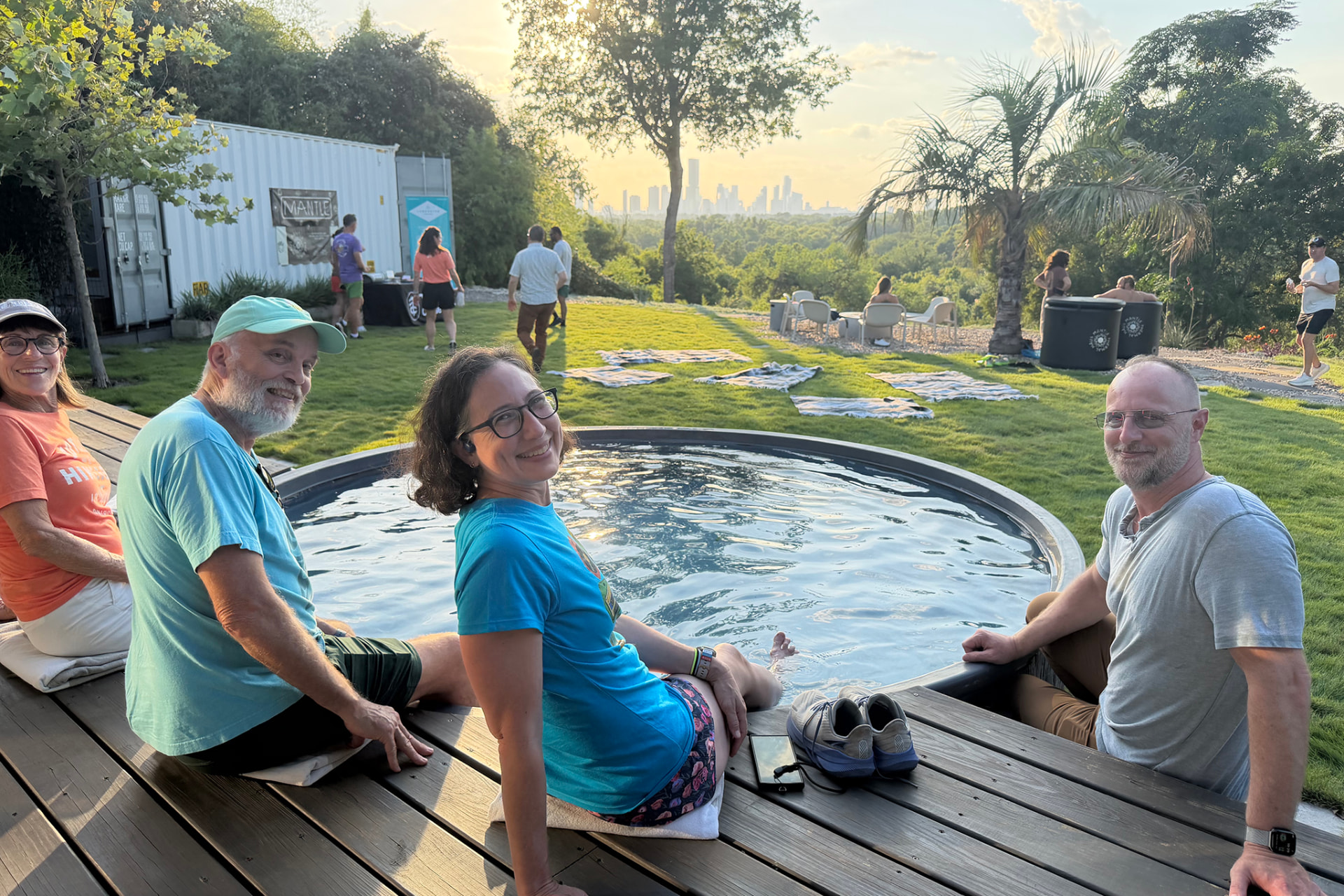 Guests around the dipping pool on the deck at golden hour, lawn and skyline beyond