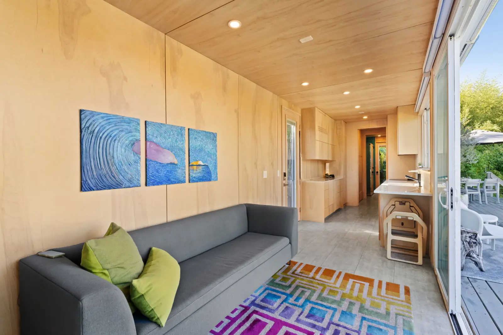 Interior lounge with wood walls, sofa, and kitchen opening onto the deck