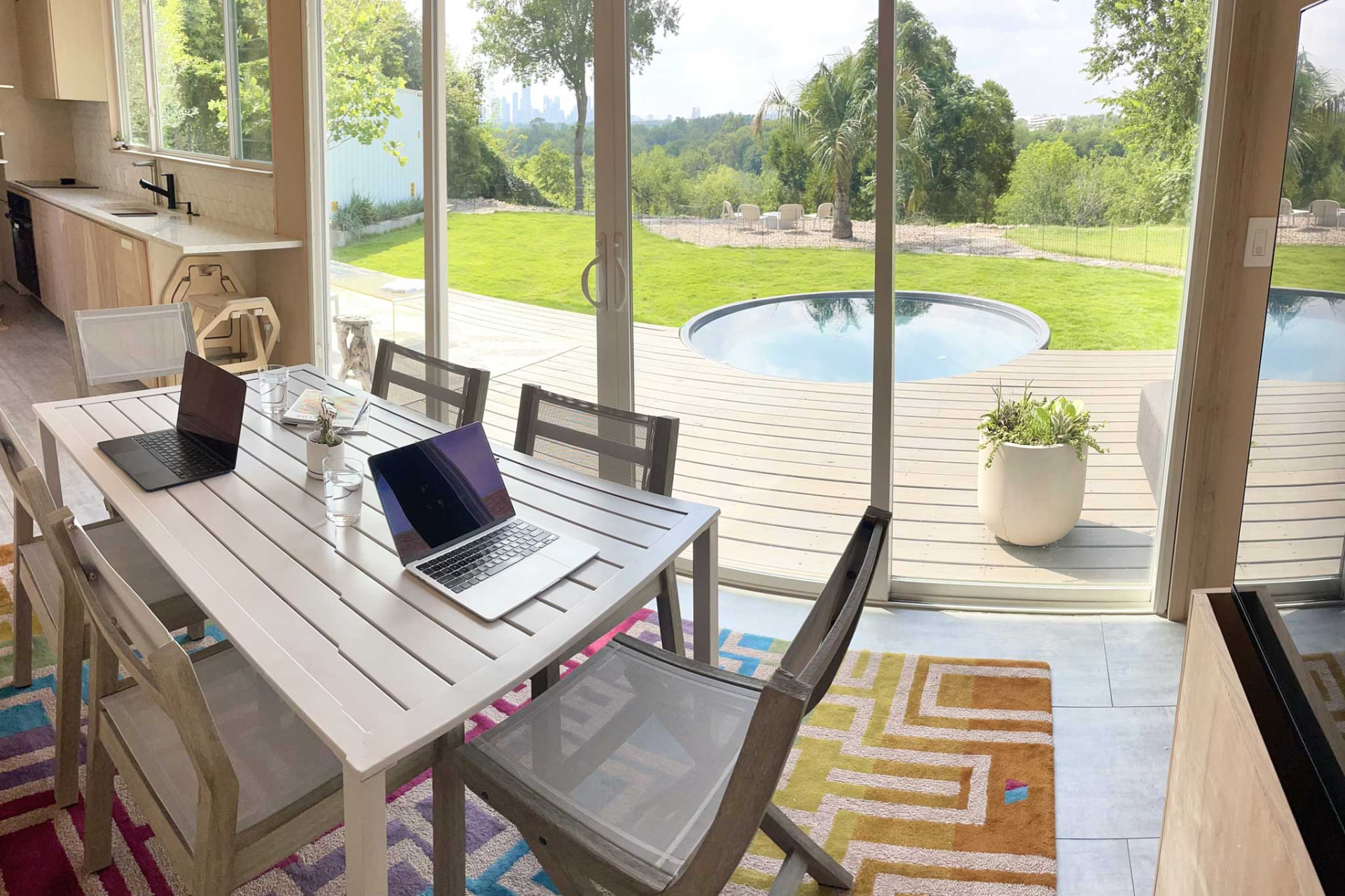 Hub interior with a long work table set for a group, kitchen counter at left, and a glass wall opening to the deck, dipping pool and downtown Austin skyline